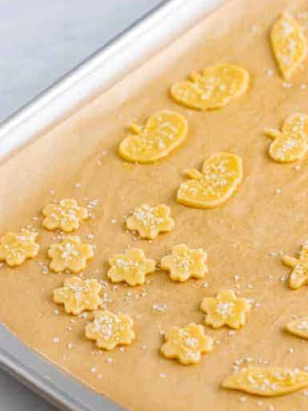 Fall shaped pie crust cutouts sprinkled with decorator sugar on a parchment lined sheet tray.