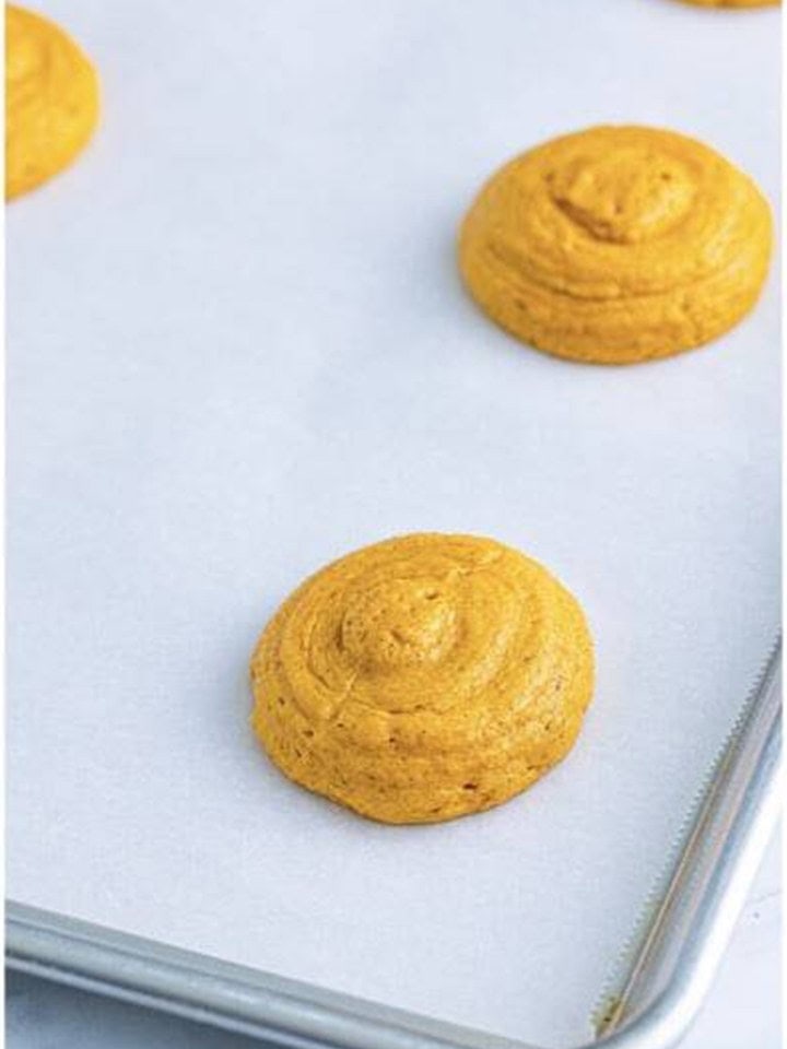Dollops of Pumpkin Whoopie Pies batter spaced apart on a parchment lined baking sheet.