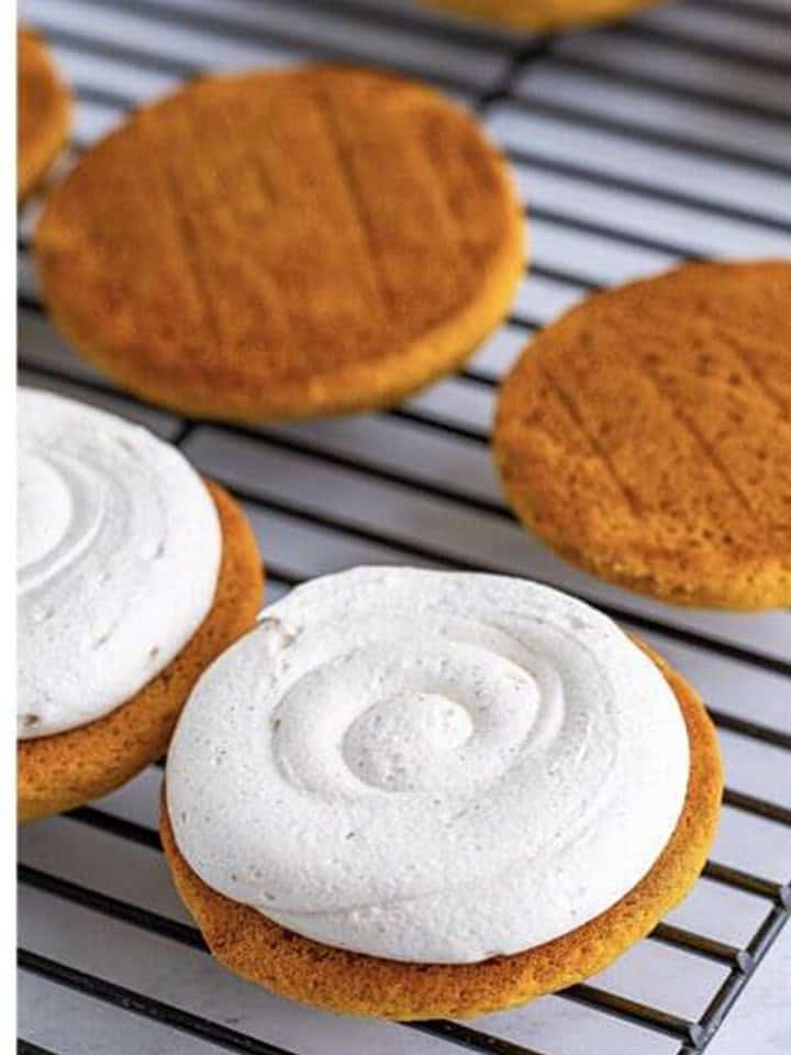 Marshmallow filling piped onto a Pumpkin Whoopie Pies cookie half on a wire rack.