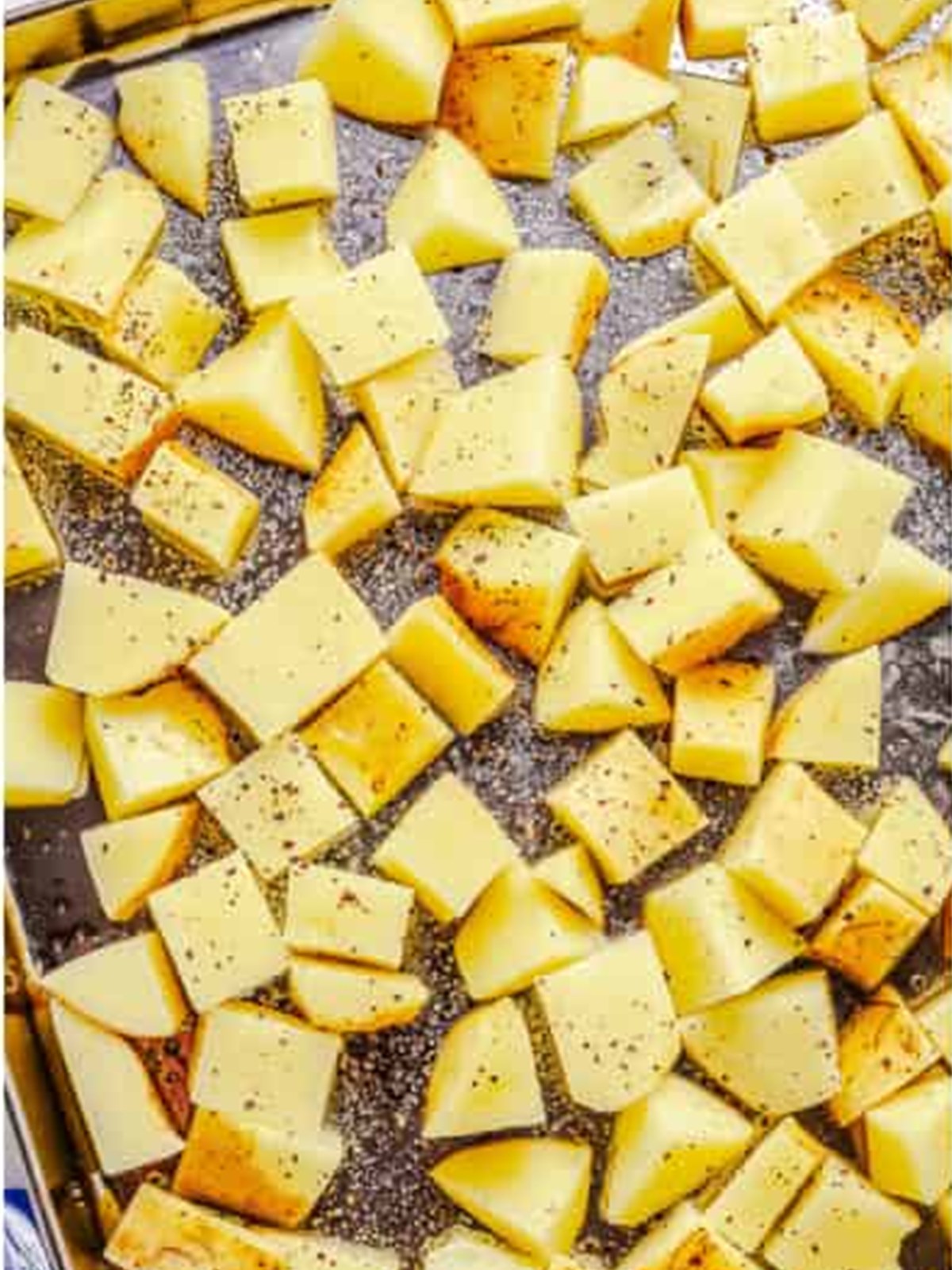Diced Yukon gold potatoes tossed with olive oil, salt, and pepper on a sheet tray.