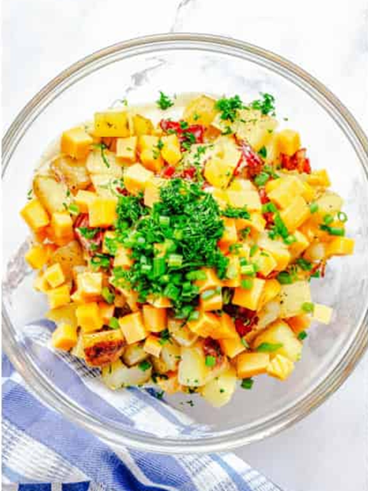 Roasted potatoes, bacon, cheddar, scallions, and herbs layered in a glass bowl with ranch dressing.