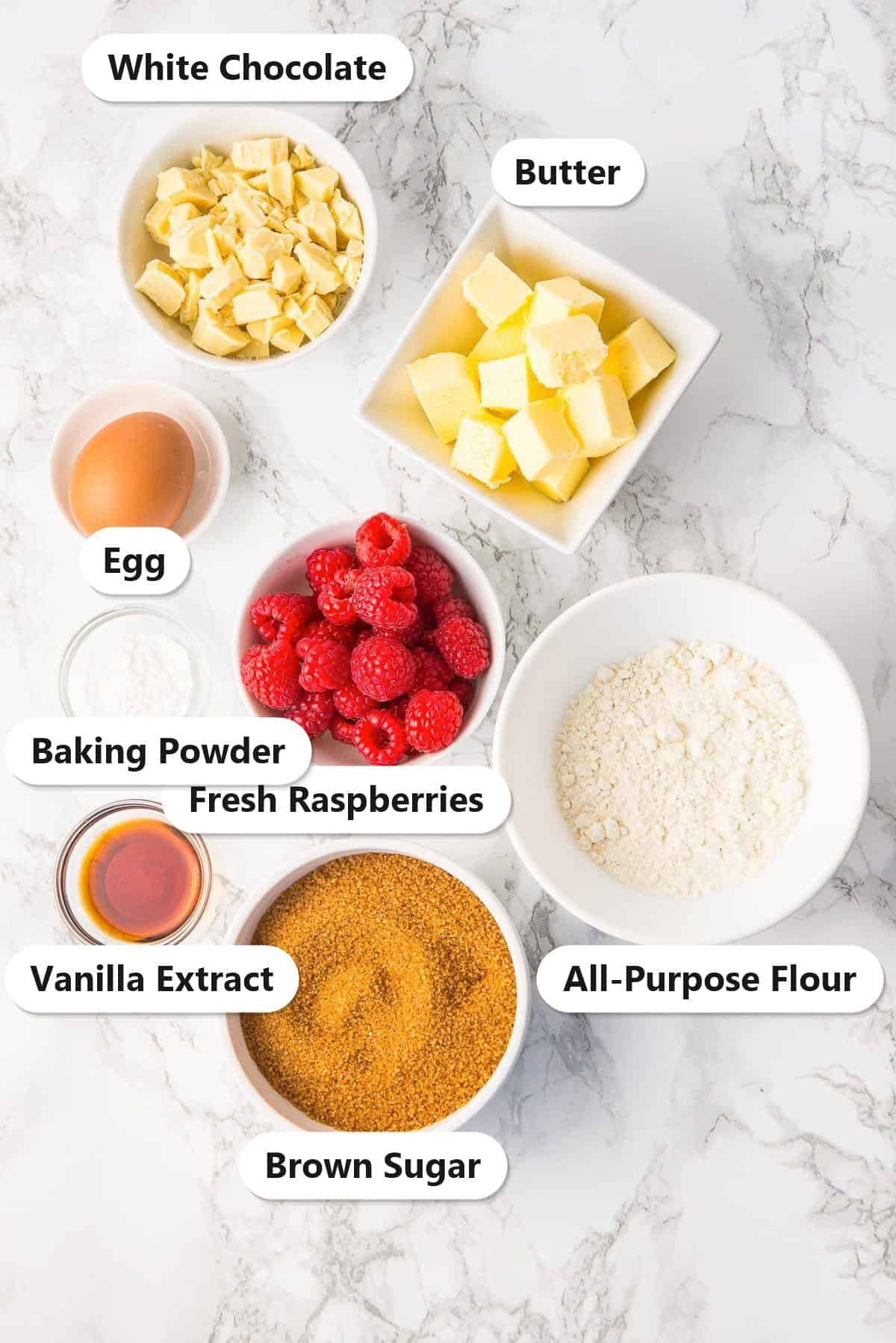 Labeled ingredients for raspberry brownies including white chocolate, butter, egg, fresh raspberries, baking powder, all-purpose flour, vanilla extract, and brown sugar.