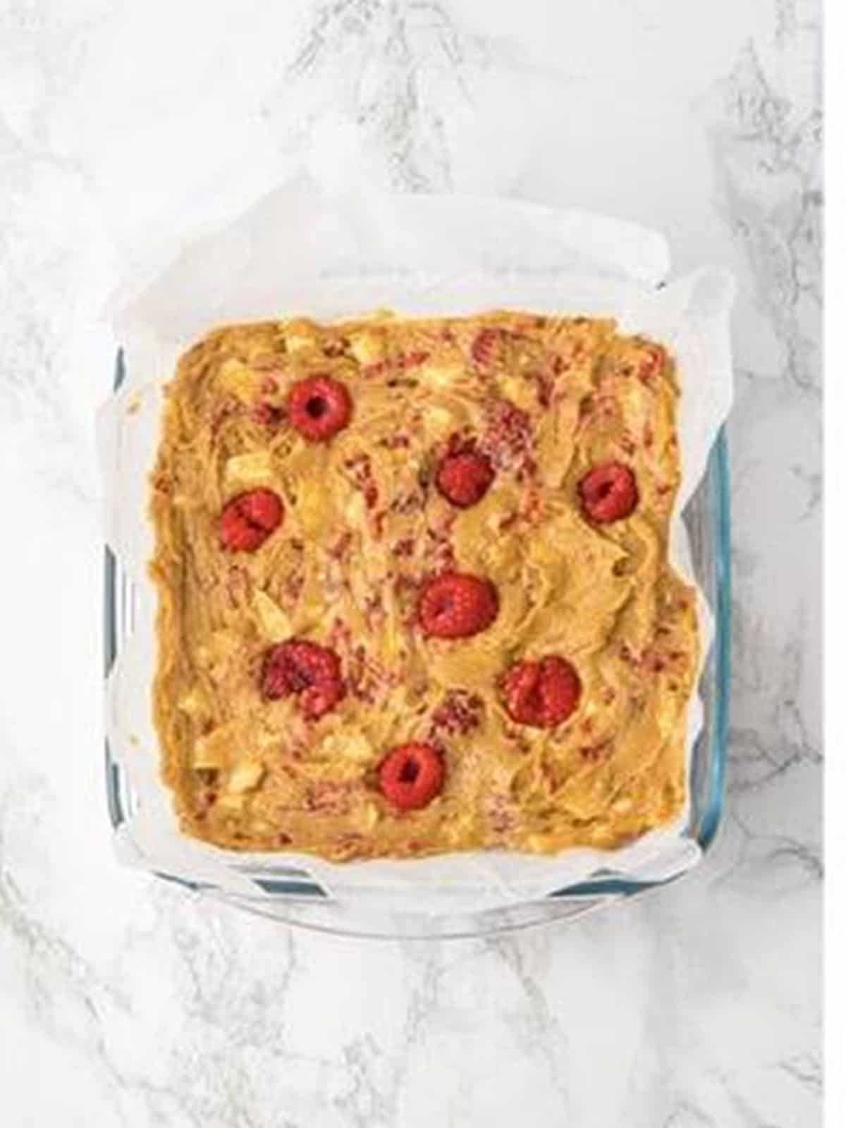 Raspberry brownies batter spread evenly in a parchment lined baking pan.