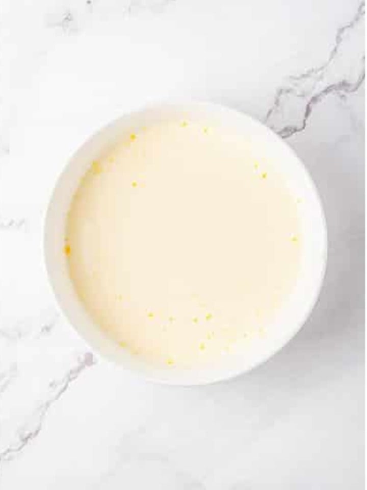 Milk and eggs whisked together in a small white bowl.