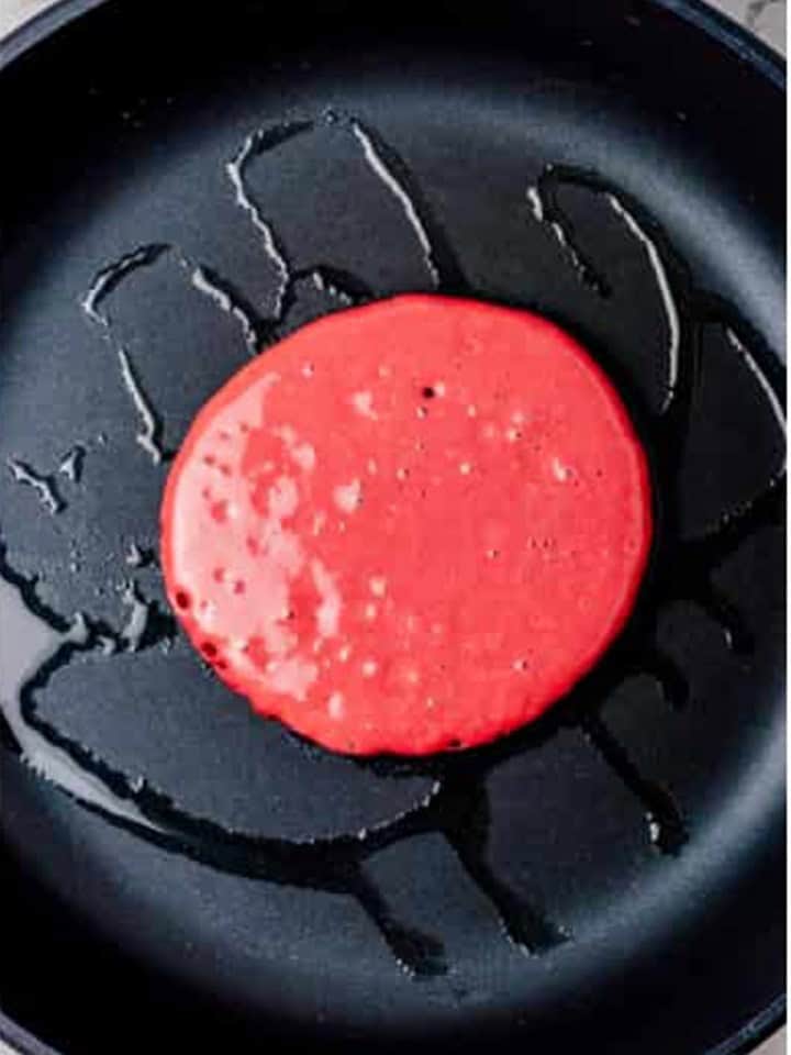 A red velvet pancake cooking on a hot nonstick skillet.