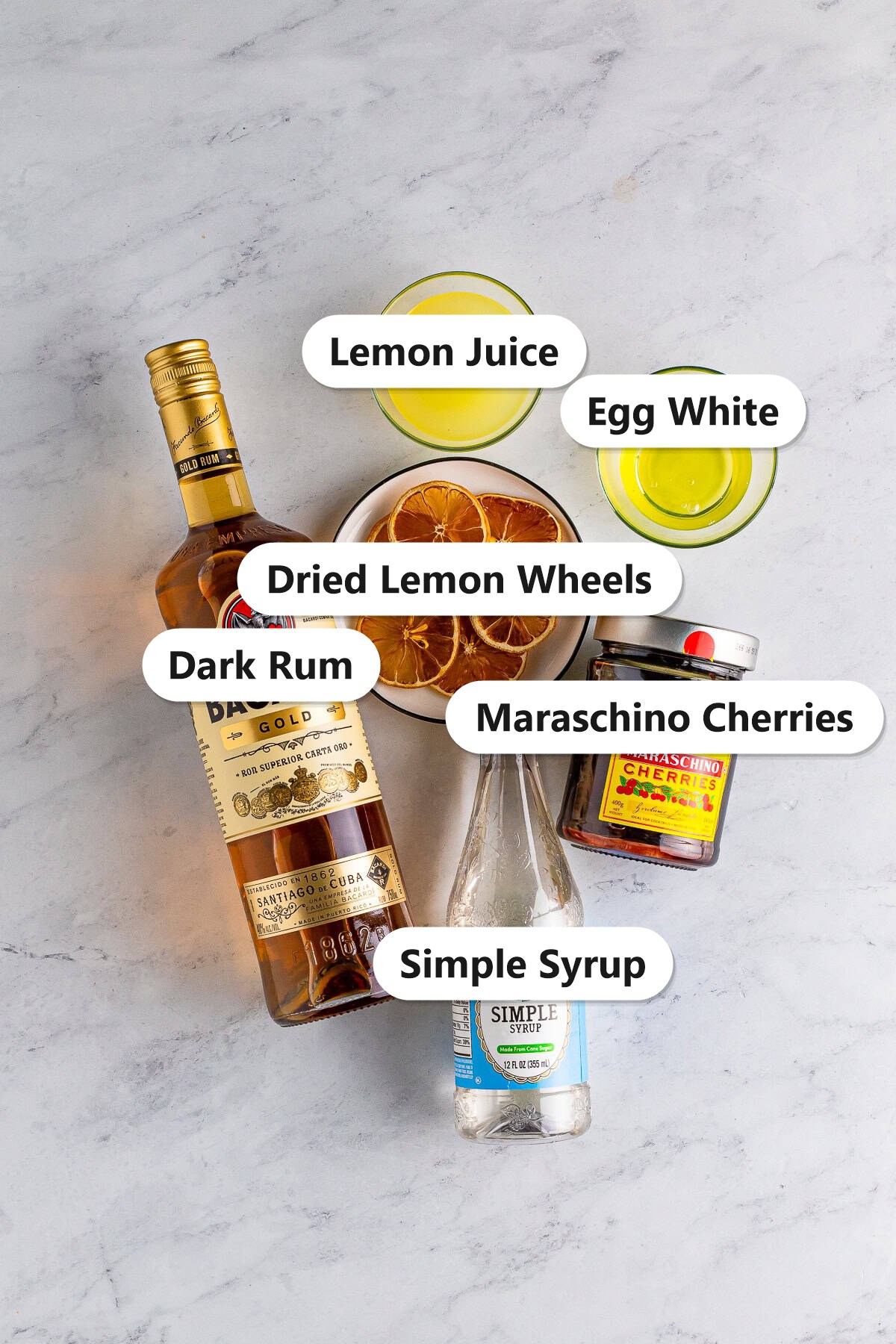 Labeled ingredients for a rum sour including dark rum, lemon juice, egg white, simple syrup, dried lemon wheels, and maraschino cherries.