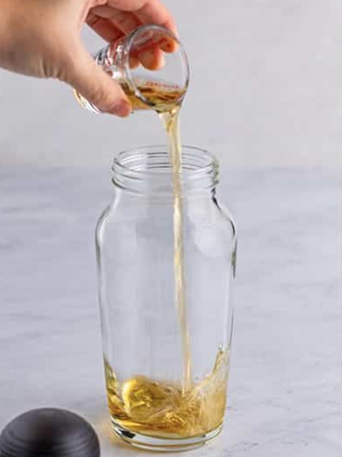 Pouring dark rum into a cocktail shaker for a rum sour.