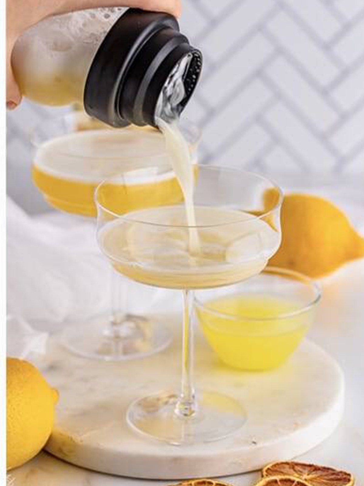 Straining the rum sour into a chilled coupe glass showing the foamy top.