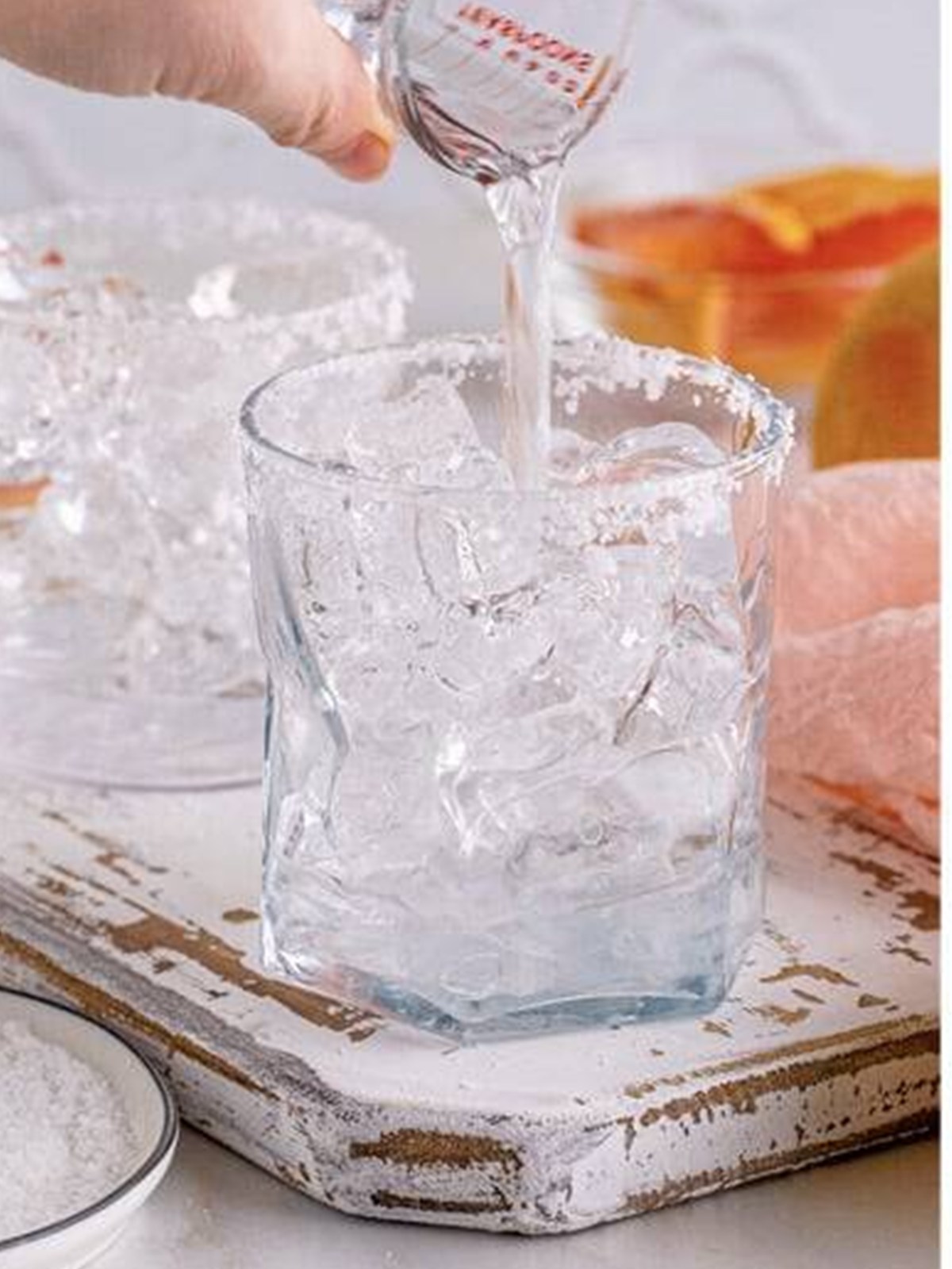 Pouring gin over ice in the salt-rimmed glass.