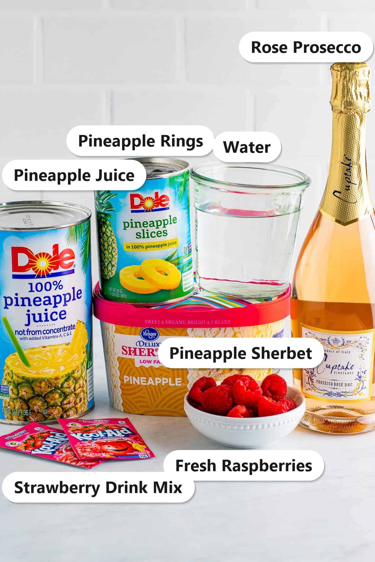 Labeled ingredients for Sherbet Punch including pineapple sherbet, pineapple juice, strawberry drink mix, rose prosecco, water, pineapple rings, and fresh raspberries.