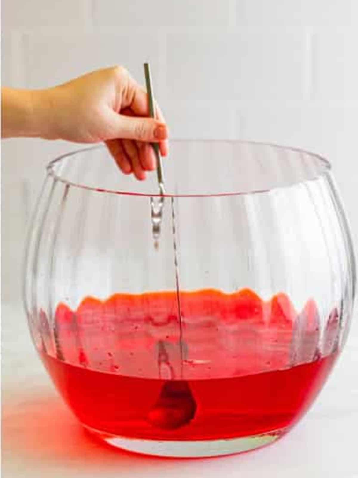Stirring the strawberry drink mix and water together in the punch bowl until dissolved.