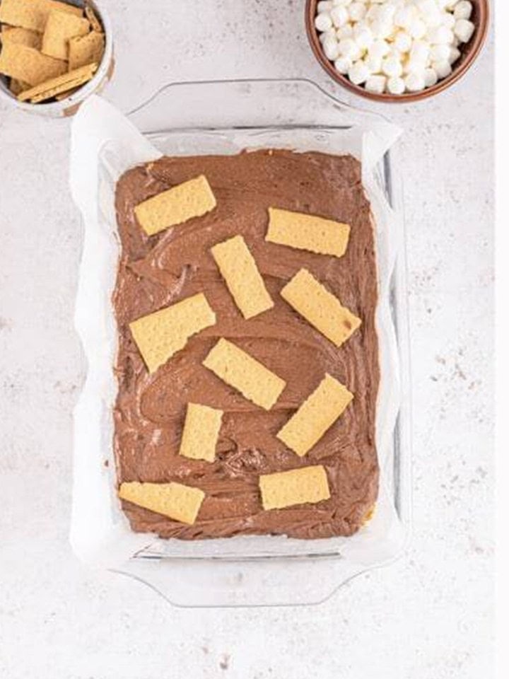 Brownie batter spread over the graham cracker crust in the baking dish.