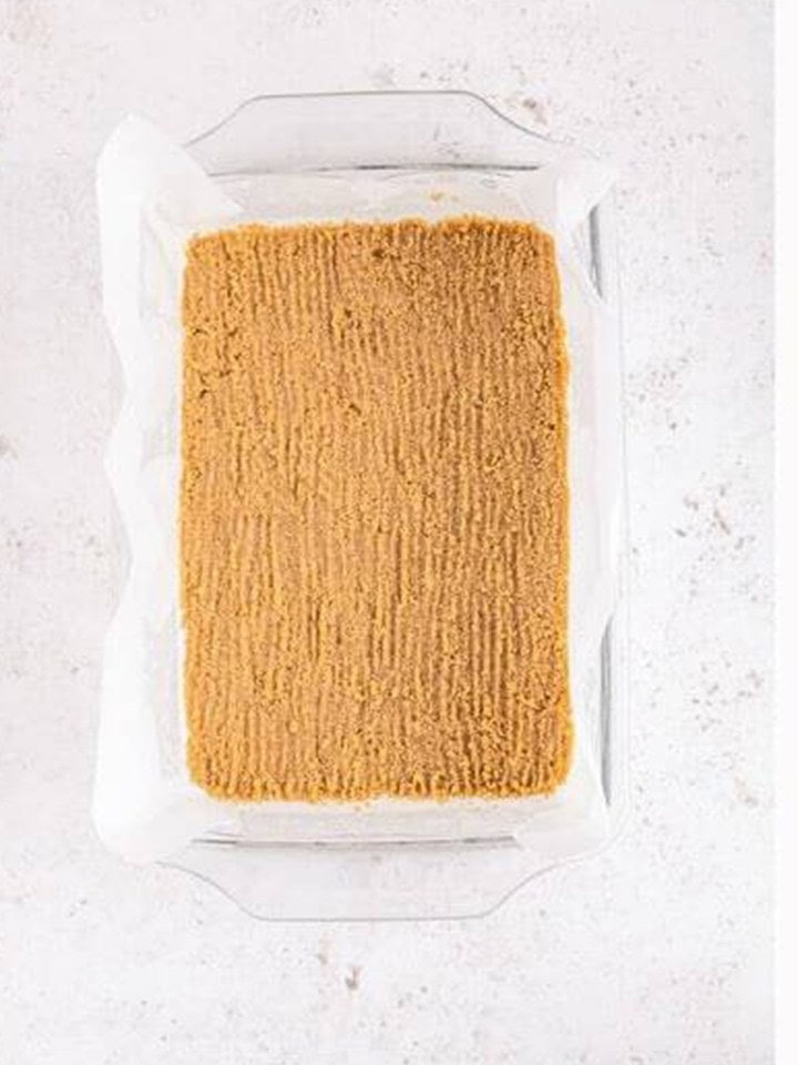 Graham cracker crust pressed evenly into a parchment lined baking dish.