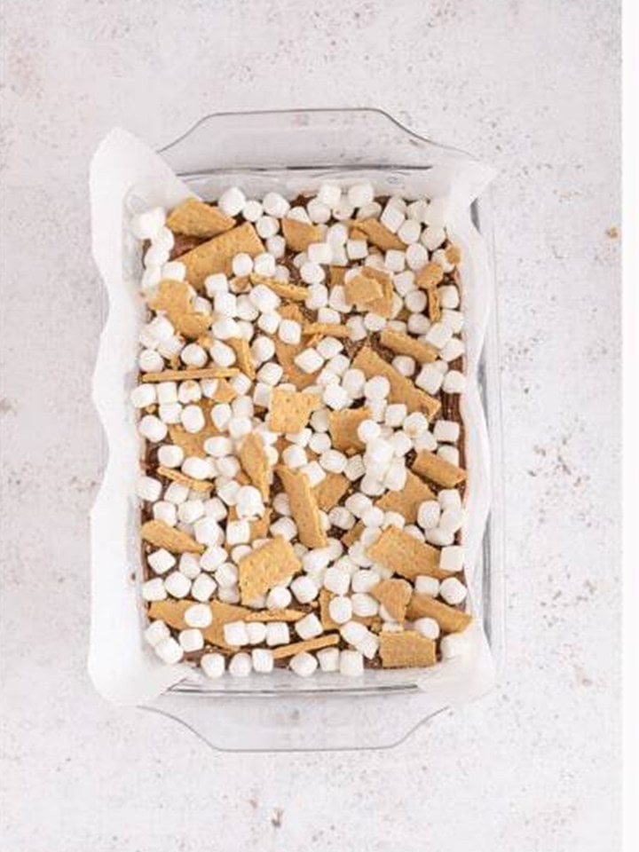 Mini marshmallows and graham cracker pieces scattered over the brownie layer before baking.