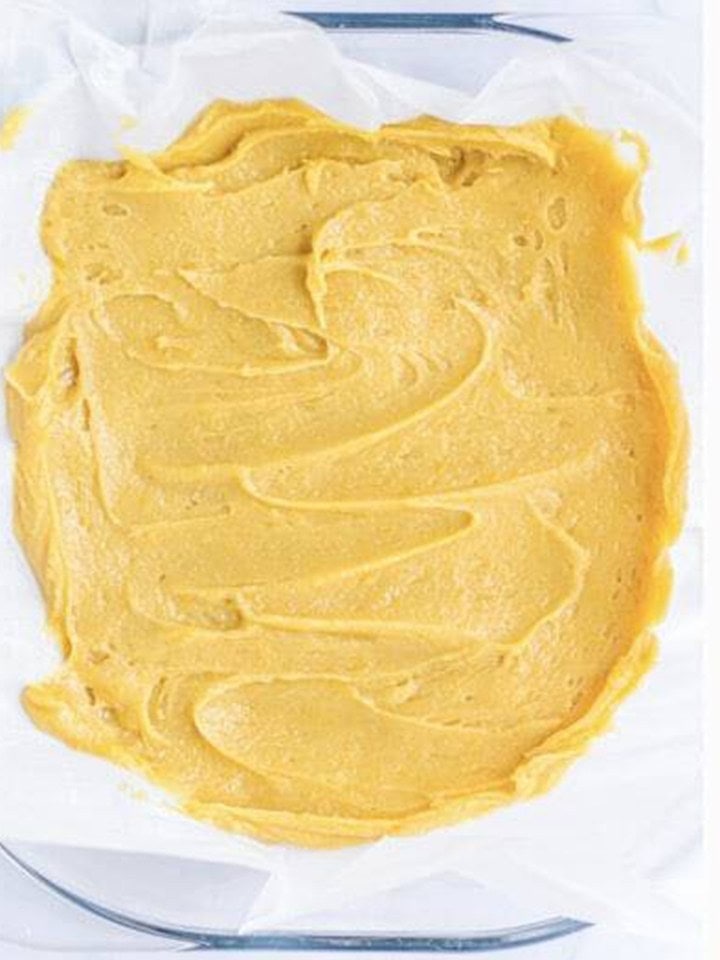 Snickerdoodle blondie batter spread evenly in a parchment lined baking dish.