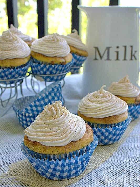 Frosted snickerdoodle cupcakes in blue gingham liners next to a bottle of milk.