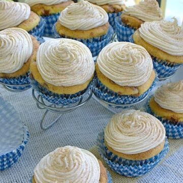 Snickerdoodle cupcakes topped with cinnamon cream cheese frosting and cinnamon sugar on a cupcake stand.