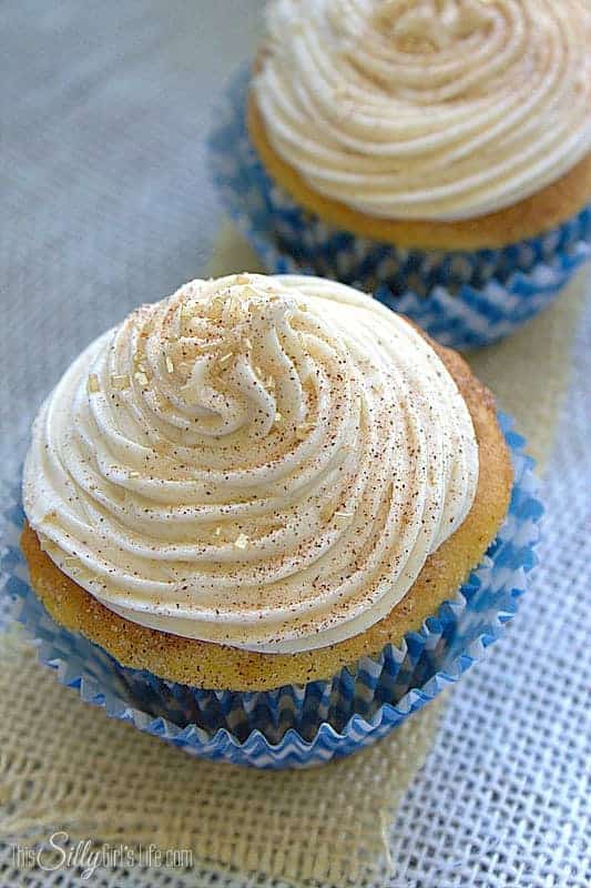 A single snickerdoodle cupcake with a tall swirl of cinnamon sugar dusted cream cheese frosting.