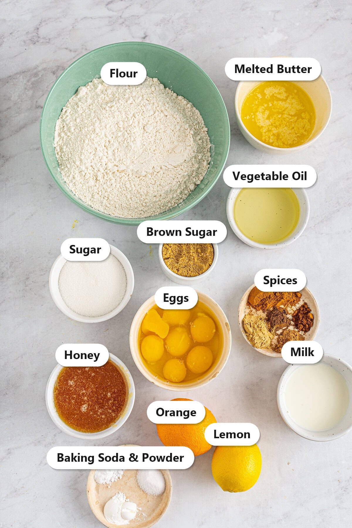 Labeled ingredients for spiced bundt cake including flour, spices, eggs, honey, brown sugar, sugar, melted butter, vegetable oil, milk, orange, lemon, and leavening.