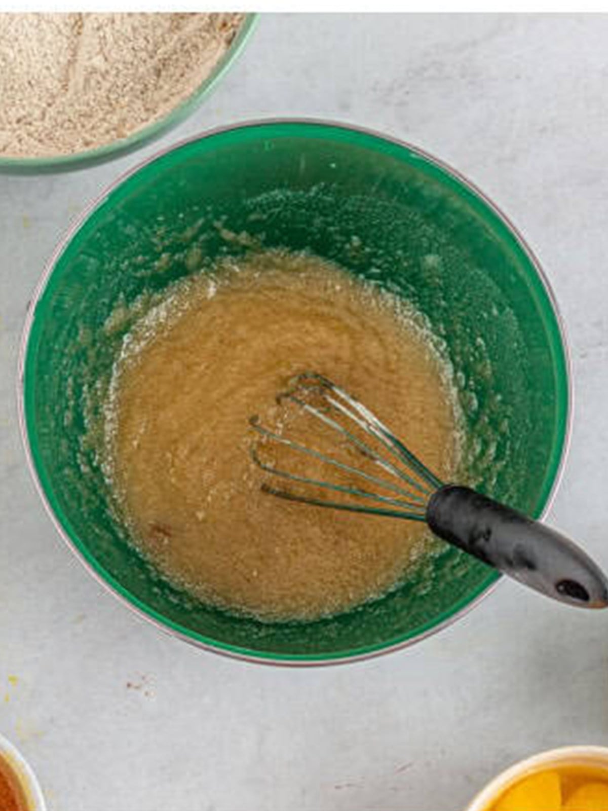 Sugar, oil, melted butter, and brown sugar whisked together in a green bowl.