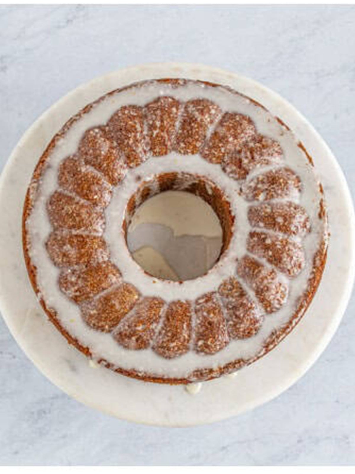 A baked spiced bundt cake drizzled with citrus glaze on a cake stand.