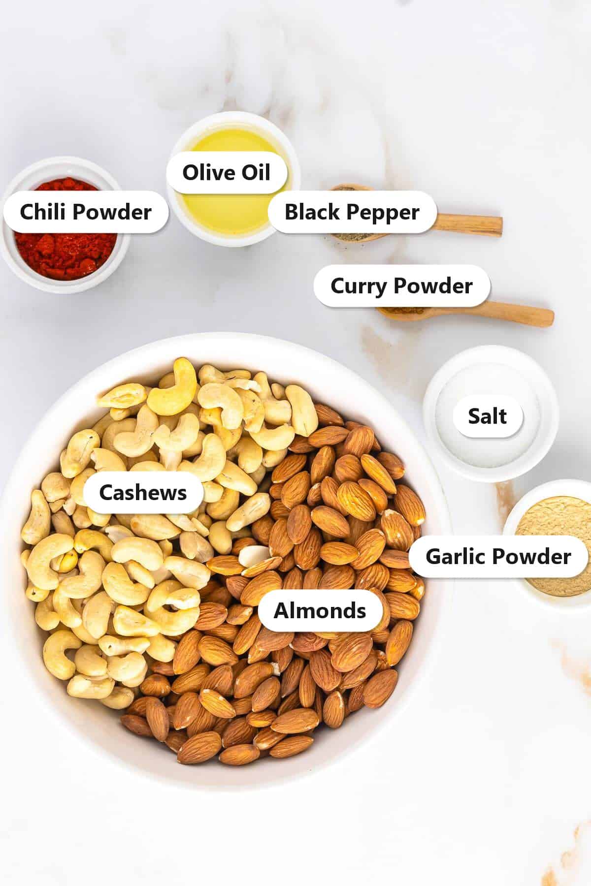 Labeled ingredients for spiced nuts including almonds, cashews, olive oil, chili powder, garlic powder, curry powder, black pepper, and salt.
