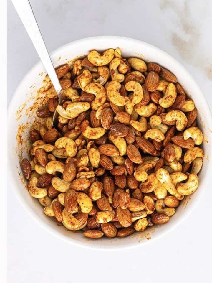 Almonds and cashews stirred until evenly coated in the spice mixture for spiced nuts.