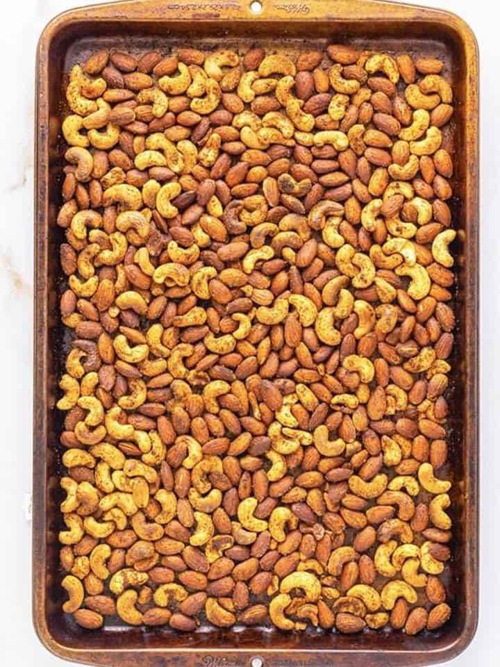 Seasoned nuts spread in a single layer on a baking sheet before roasting for spiced nuts.