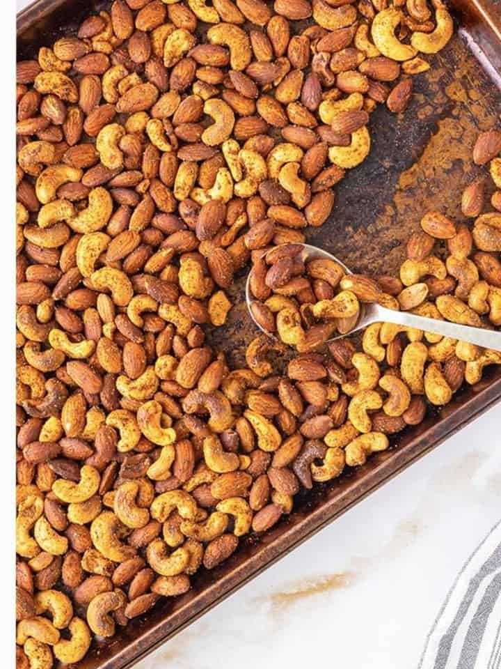 Roasted spiced nuts on the baking sheet being stirred with a spoon after baking.