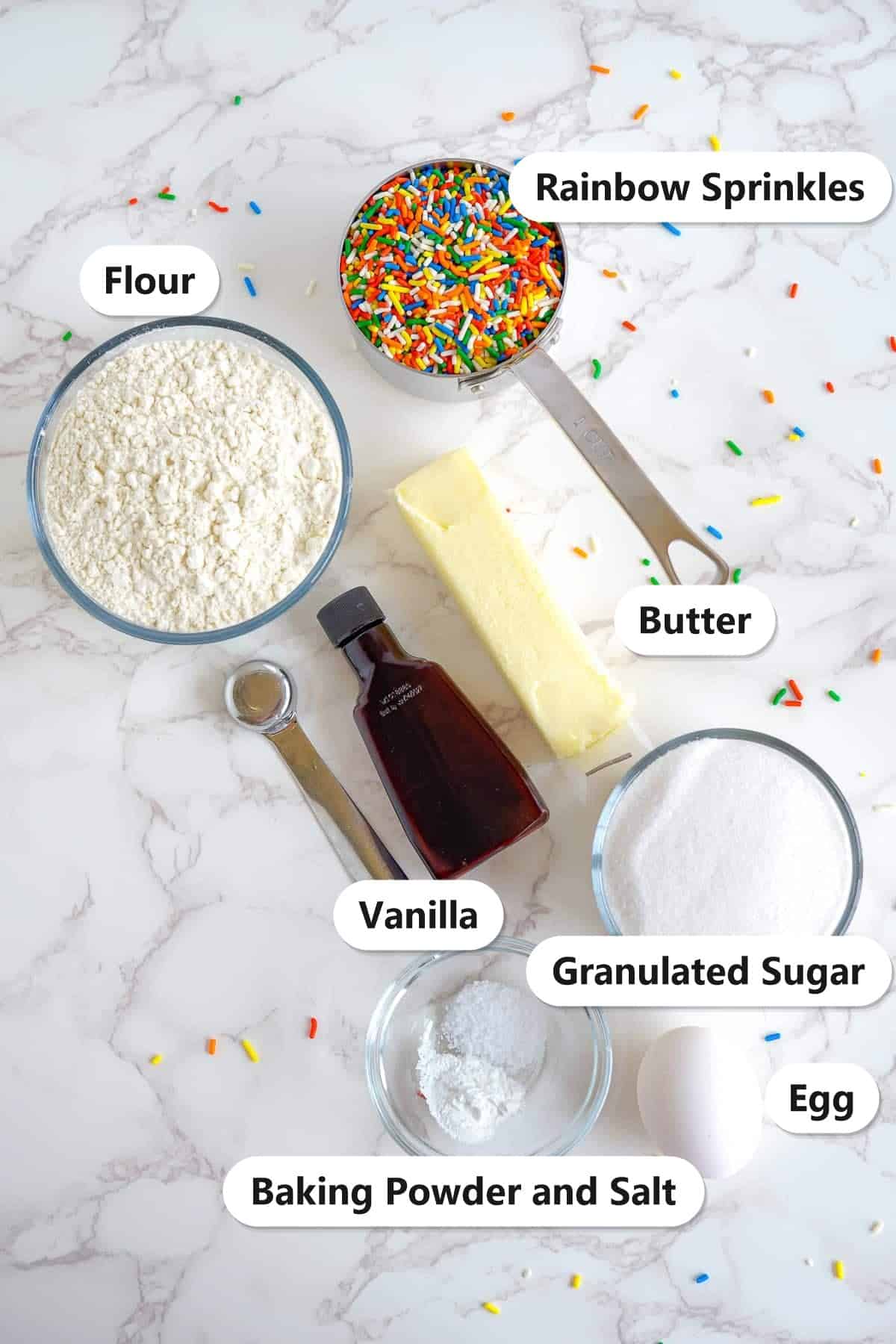 Labeled ingredients for Sprinkle Cookies including flour, butter, granulated sugar, rainbow sprinkles, vanilla, egg, baking powder, and salt.