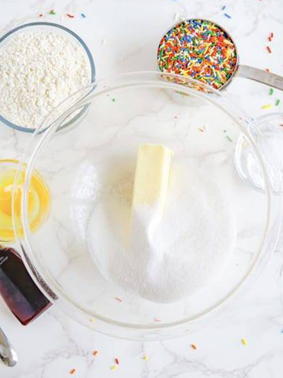 Butter, sugar, vanilla, and egg staged in a glass mixing bowl for Sprinkle Cookies.