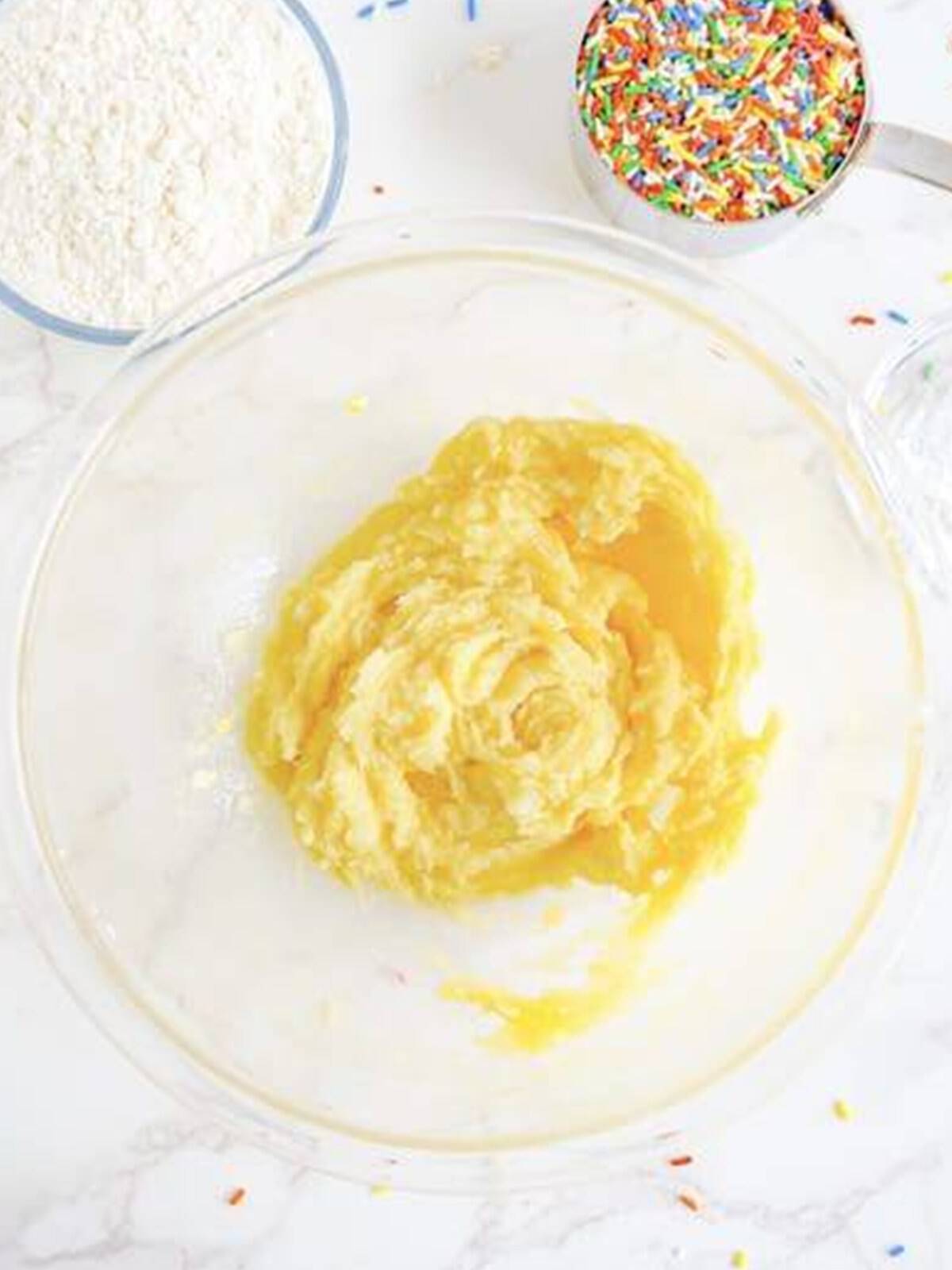 Butter, sugar, egg, and vanilla creamed smooth in a glass mixing bowl.