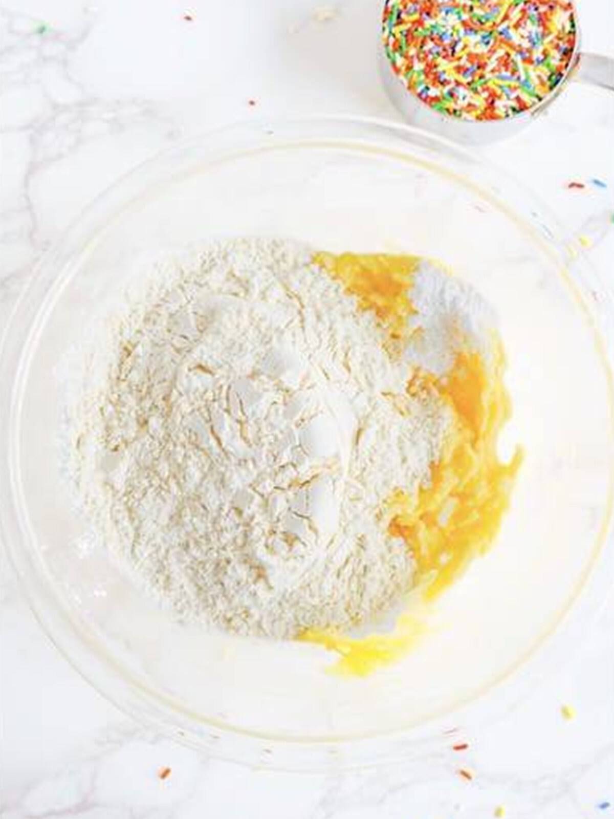 Flour, baking powder, and salt added on top of the creamed mixture in a glass bowl.
