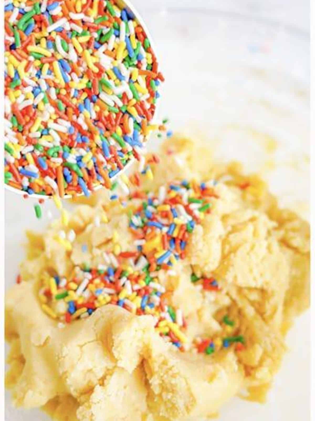 Rainbow sprinkles poured into the sugar cookie dough in a glass bowl.