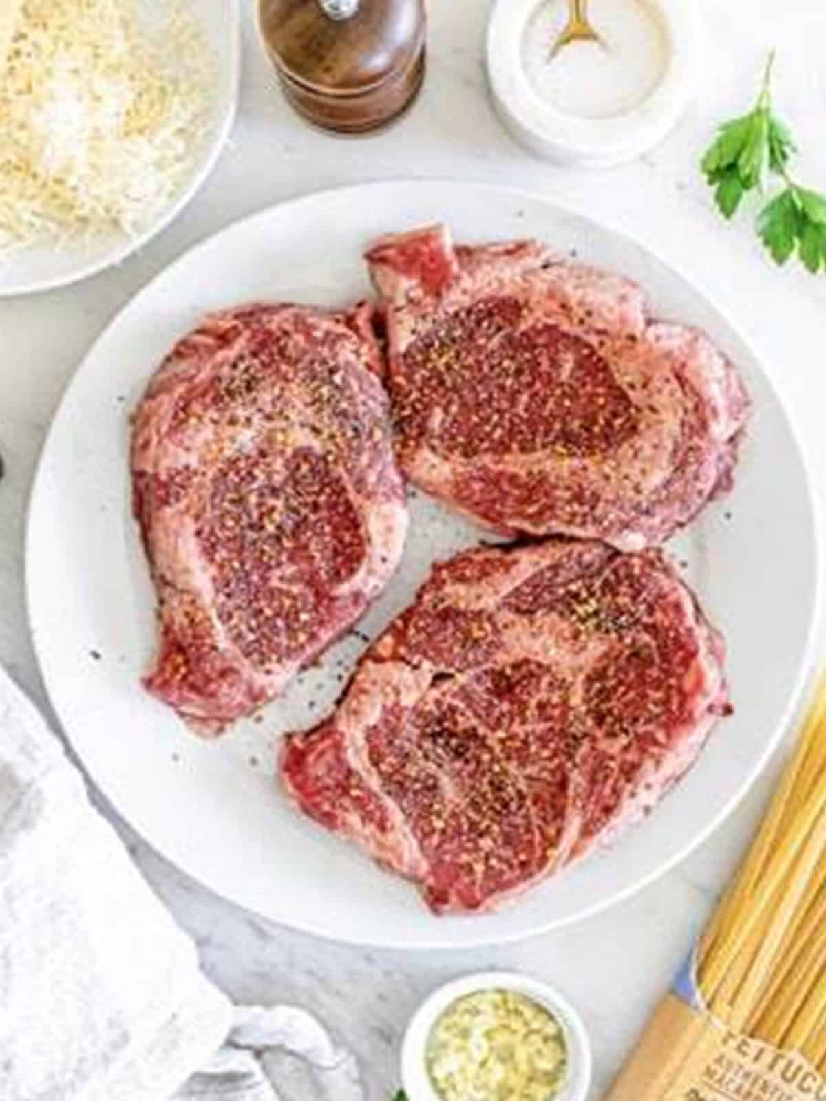 Ribeye steaks seasoned on both sides with steak seasoning for Steak Alfredo.