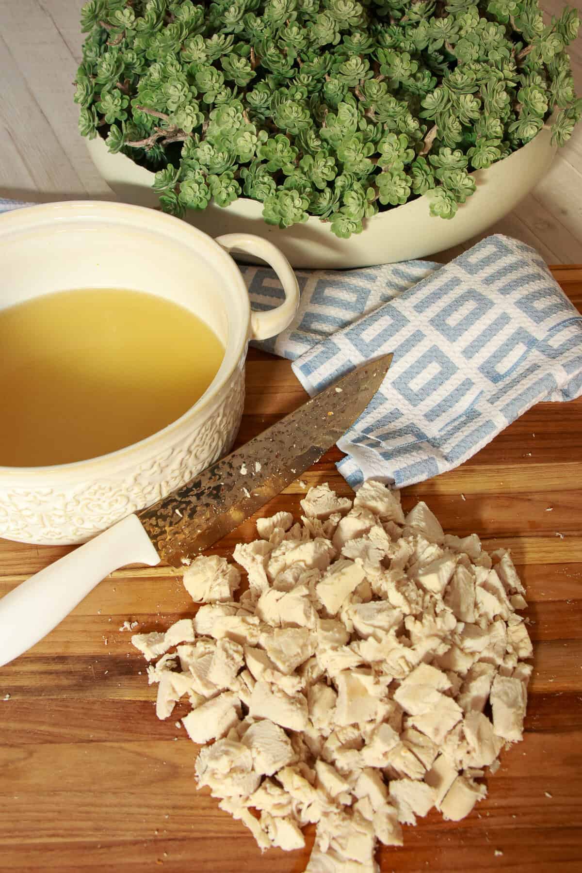 Diced cooked chicken on a cutting board next to strained chicken stock and fresh thyme.
