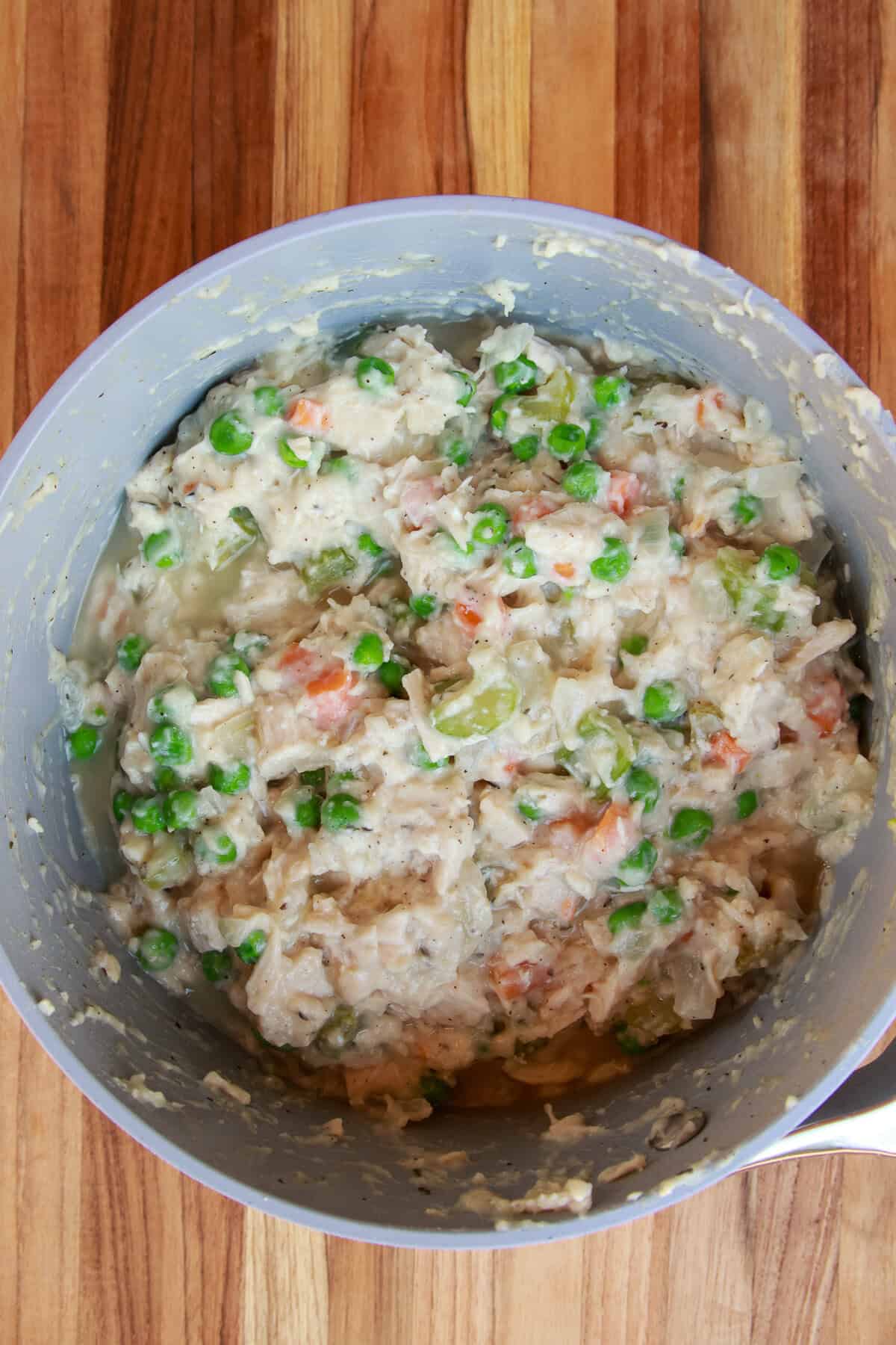 Creamy chicken pot pie filling with peas and vegetables stirred together in a pot.