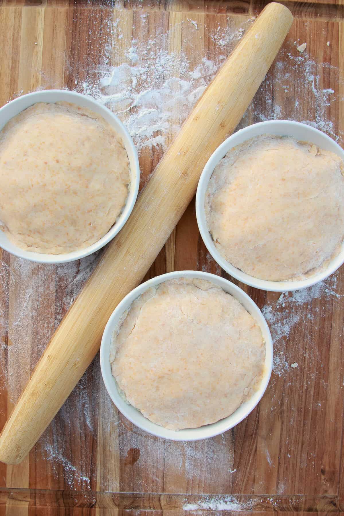 Rolled cheesy crust dough draped over the pot pie dishes with a rolling pin.