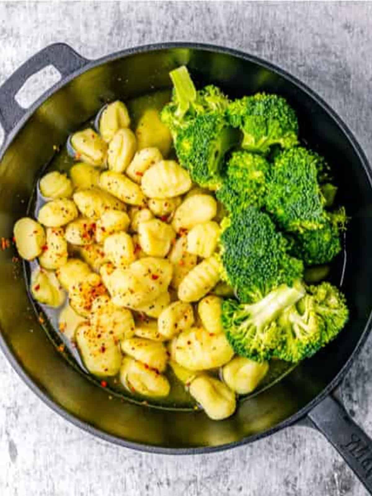 Gnocchi and broccoli florets with red pepper flakes and seasoning in a cast iron skillet