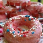 Close up of a glazed strawberry donut covered in white sprinkles