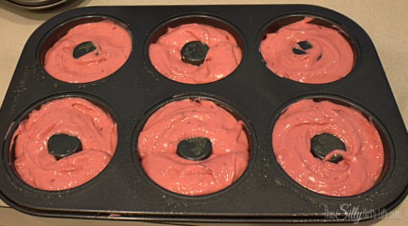 Pink strawberry donut batter spooned into a greased donut pan