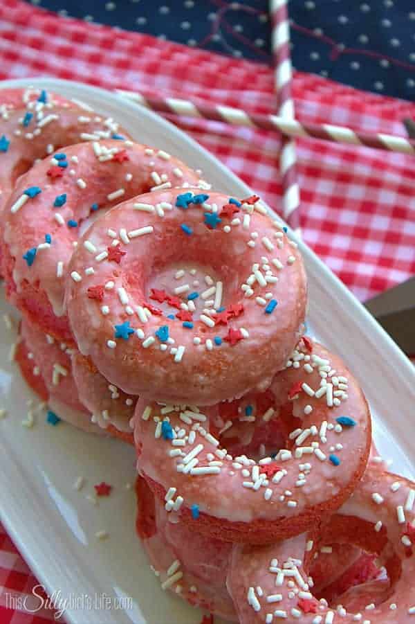 Glazed strawberry donuts topped with sprinkles stacked on a white platter