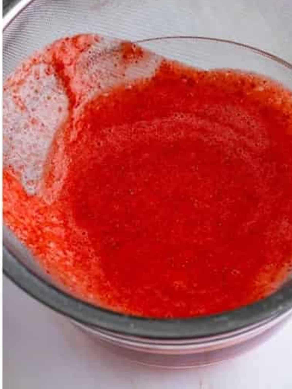 Strawberry puree being pressed through a fine mesh sieve to remove the seeds for Strawberry Ice Cream.