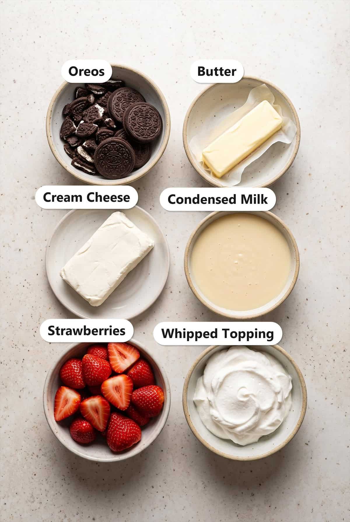 Labeled ingredients for strawberry icebox cake bars including Oreos, butter, cream cheese, sweetened condensed milk, strawberries, and whipped topping.
