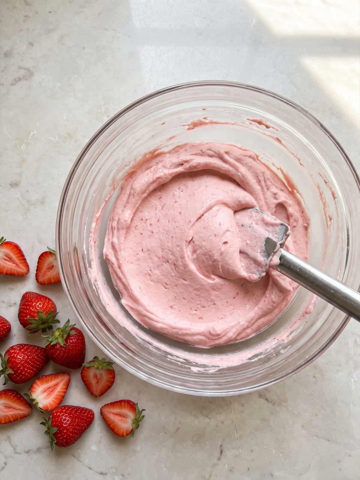 A fluffy pink strawberry cream cheese filling folded in a glass bowl.