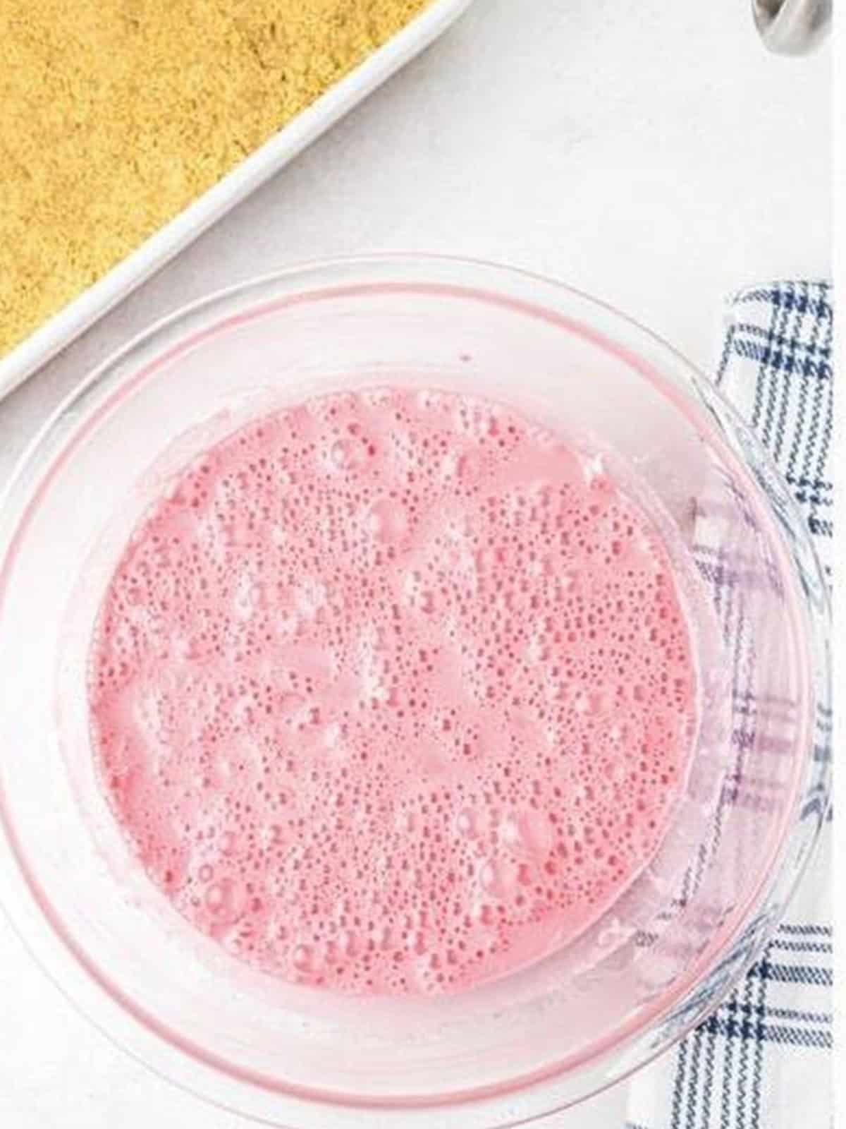 Strawberry jello mixture combined into the cream cheese filling in a glass bowl.