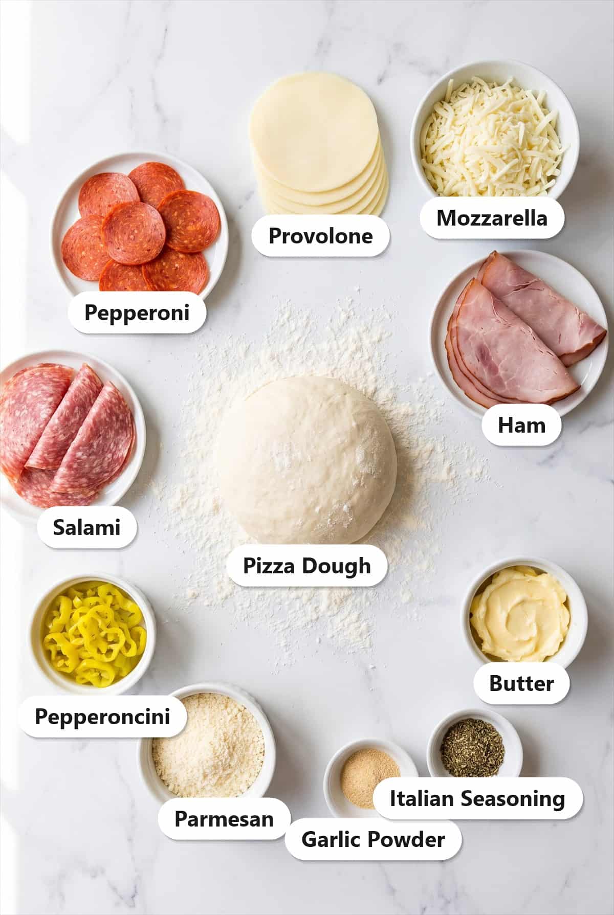 Ingredients to make stromboli: pizza dough, pepperoni, hard salami, deli ham, provolone, shredded mozzarella, pepperoncini, parmesan, butter, garlic powder, and Italian seasoning.
