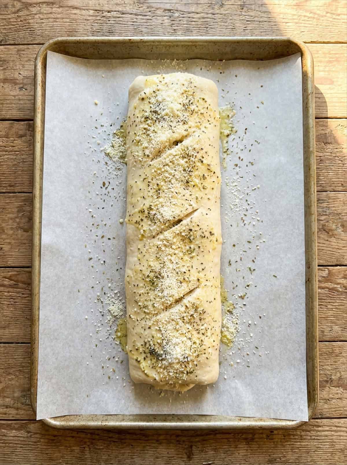 Unbaked stromboli log brushed with garlic butter and sprinkled with parmesan on a parchment lined baking sheet.