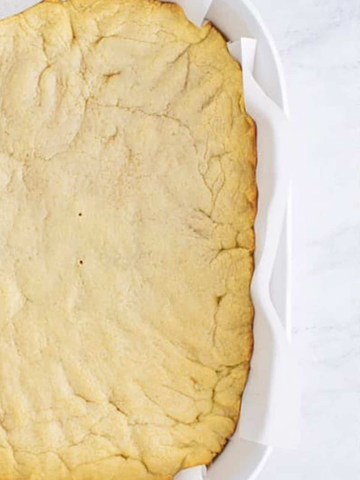 Baked sugar cookie bar base golden in a parchment lined pan.