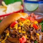 A Taco Joes sandwich piled high with saucy taco beef, melted cheddar, and diced tomatoes on a soft bun.